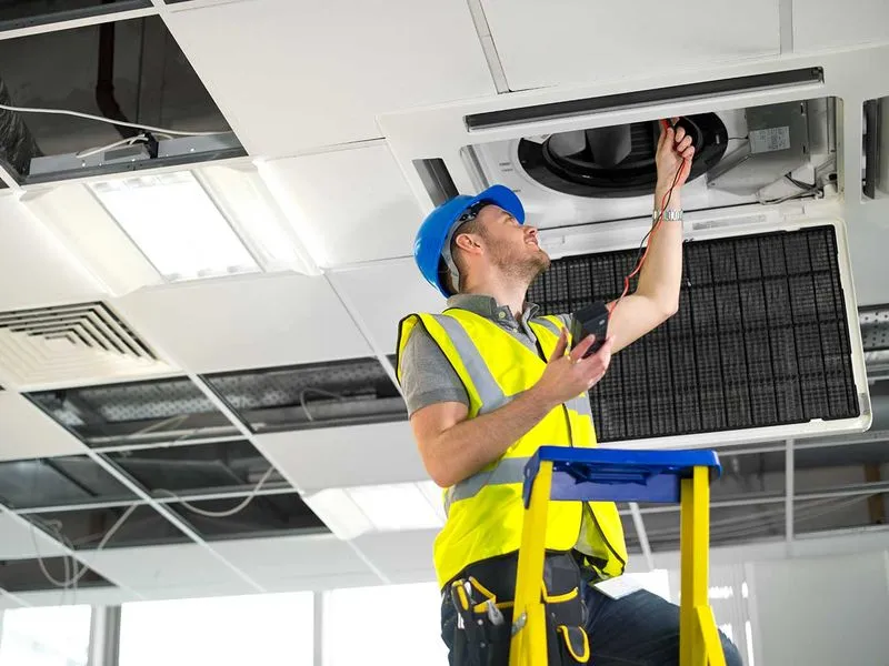 Techniker mit Schutzhelm und Warnweste überprüft eine technische Anlage.